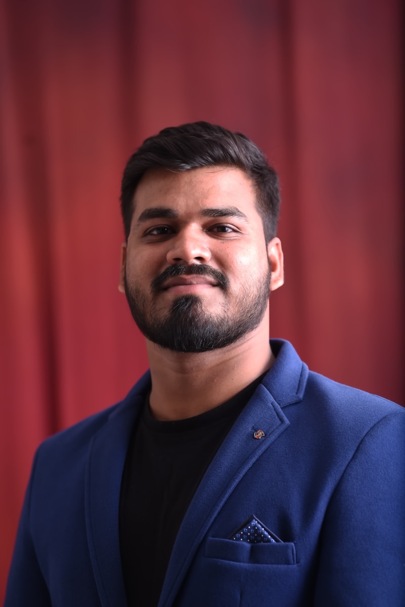 A man in a blue suit standing in front of a red curtain